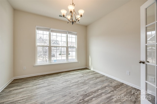 spare room featuring baseboards, an inviting chandelier, and wood finished floors