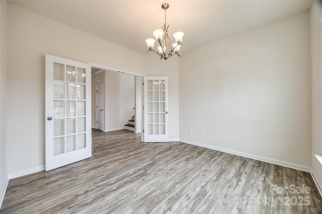 spare room featuring french doors, baseboards, a notable chandelier, and wood finished floors