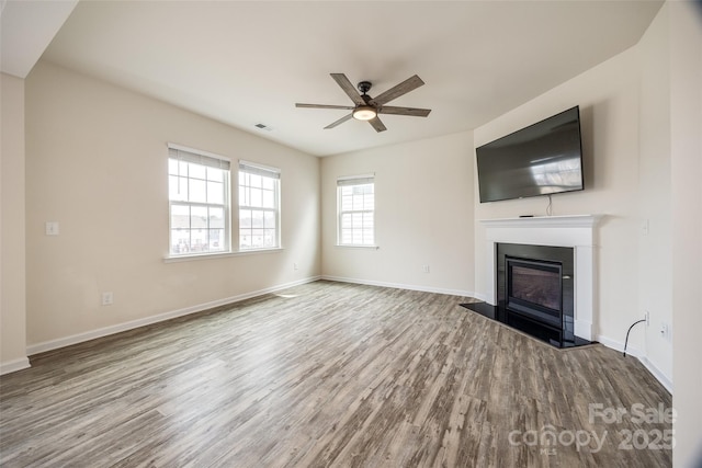 unfurnished living room featuring visible vents, baseboards, wood finished floors, a glass covered fireplace, and a ceiling fan