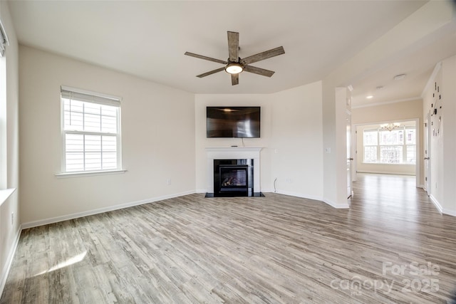 unfurnished living room featuring a fireplace with flush hearth, ceiling fan with notable chandelier, baseboards, and wood finished floors