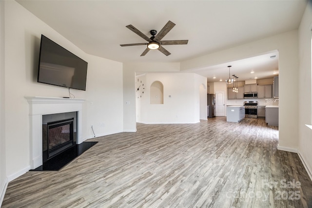 unfurnished living room featuring baseboards, ceiling fan, wood finished floors, a glass covered fireplace, and a sink