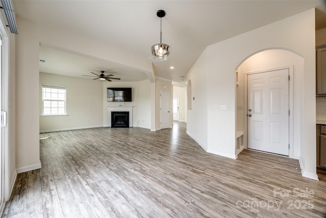 unfurnished living room with light wood-style flooring, a fireplace, baseboards, and ceiling fan