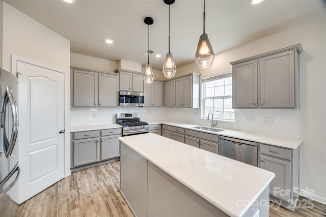 kitchen featuring gray cabinetry, decorative backsplash, light wood-style floors, stainless steel appliances, and a sink