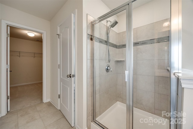 full bath featuring tile patterned floors, a stall shower, a walk in closet, and baseboards