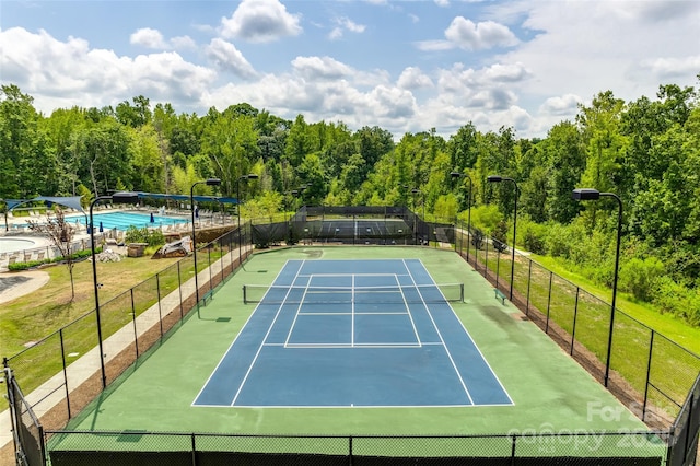 view of sport court with a wooded view and fence