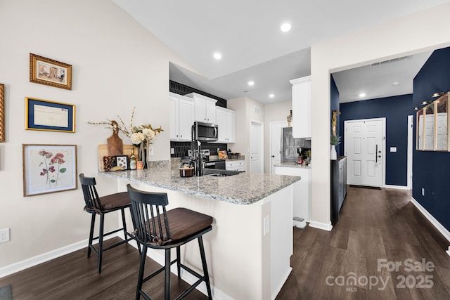 kitchen featuring light stone counters, stainless steel microwave, dark wood-type flooring, white cabinets, and a peninsula