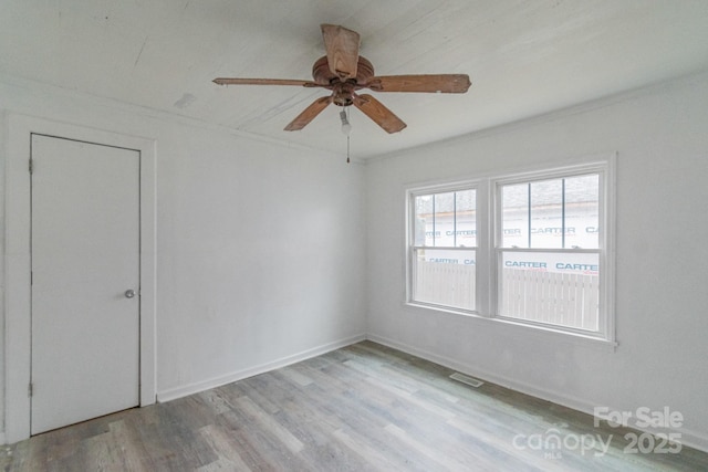 empty room with wood finished floors, a ceiling fan, and baseboards