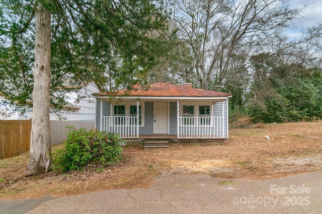 bungalow featuring a porch, metal roof, fence, and a standing seam roof