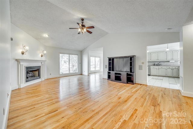 unfurnished living room with baseboards, light wood finished floors, a fireplace, a sink, and ceiling fan