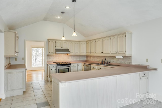 kitchen featuring cream cabinetry, under cabinet range hood, a sink, stainless steel appliances, and a peninsula