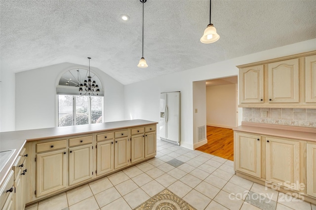 kitchen with light countertops, lofted ceiling, hanging light fixtures, white refrigerator with ice dispenser, and light tile patterned flooring