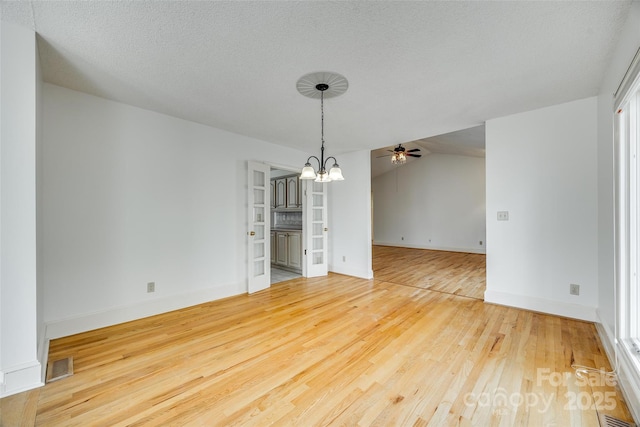 spare room featuring visible vents, vaulted ceiling, ceiling fan with notable chandelier, wood finished floors, and a textured ceiling