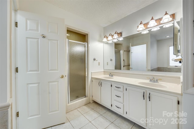 full bath featuring tile patterned flooring, a shower stall, a textured ceiling, and a sink