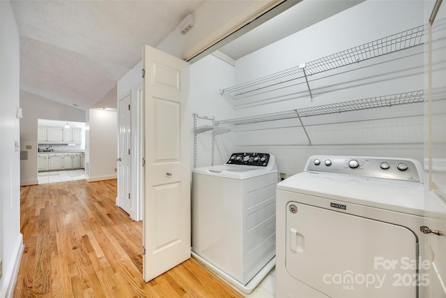 laundry room with light wood finished floors, laundry area, washer and dryer, and a textured ceiling