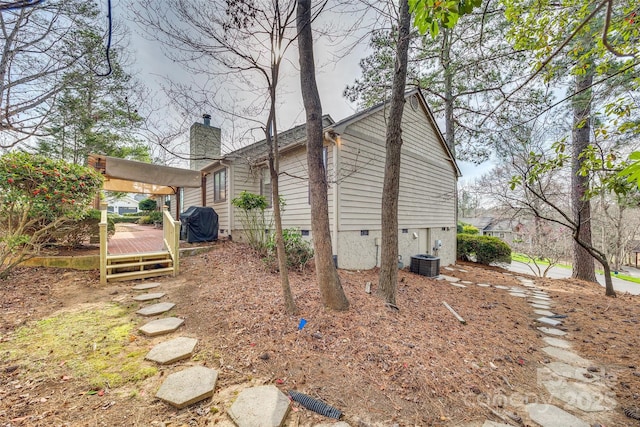 view of property exterior featuring a deck, crawl space, cooling unit, and a chimney