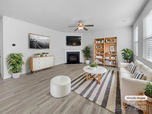 living area featuring ceiling fan, wood finished floors, and a fireplace with flush hearth