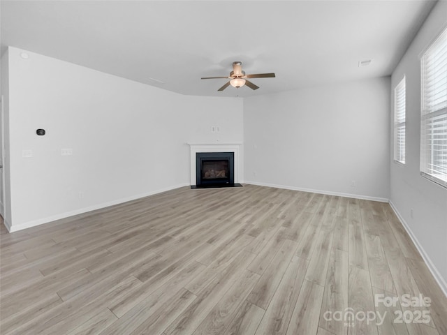 unfurnished living room featuring a fireplace with flush hearth, baseboards, ceiling fan, and light wood finished floors