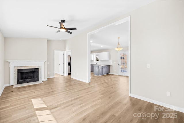 unfurnished living room with light wood finished floors, baseboards, a ceiling fan, lofted ceiling, and a premium fireplace