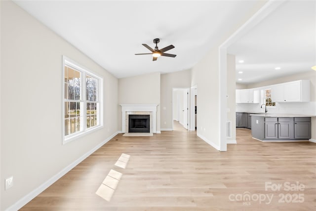 unfurnished living room with a fireplace, light wood-style flooring, vaulted ceiling, a sink, and baseboards