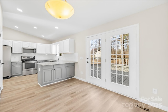 kitchen featuring lofted ceiling, light wood-style flooring, gray cabinets, stainless steel appliances, and a sink