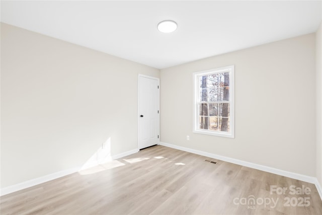 empty room with light wood-style floors, visible vents, and baseboards