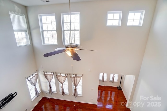 unfurnished living room with a high ceiling, wood finished floors, visible vents, baseboards, and a ceiling fan