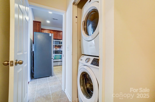 laundry room featuring light tile patterned floors, stacked washing maching and dryer, and visible vents