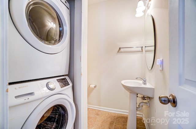 laundry area featuring stacked washer / dryer, laundry area, baseboards, and tile patterned floors