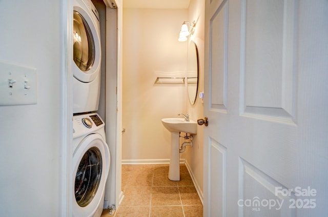 clothes washing area featuring light tile patterned floors, laundry area, stacked washing maching and dryer, and baseboards