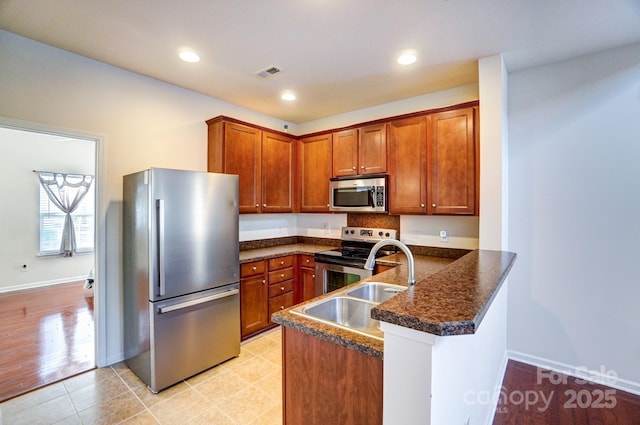 kitchen with stainless steel appliances, a peninsula, a sink, visible vents, and dark countertops