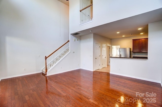 unfurnished living room featuring recessed lighting, wood finished floors, baseboards, and stairs