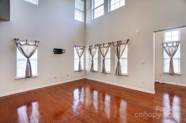 unfurnished room featuring a high ceiling, baseboards, and hardwood / wood-style flooring