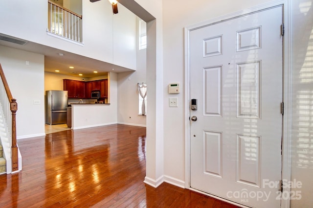 foyer entrance featuring a ceiling fan, dark wood-style flooring, a towering ceiling, and baseboards