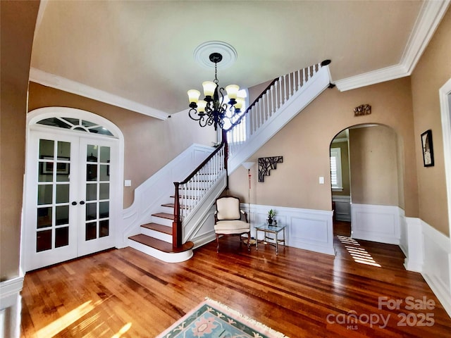 foyer entrance featuring arched walkways, a notable chandelier, wood finished floors, french doors, and stairway