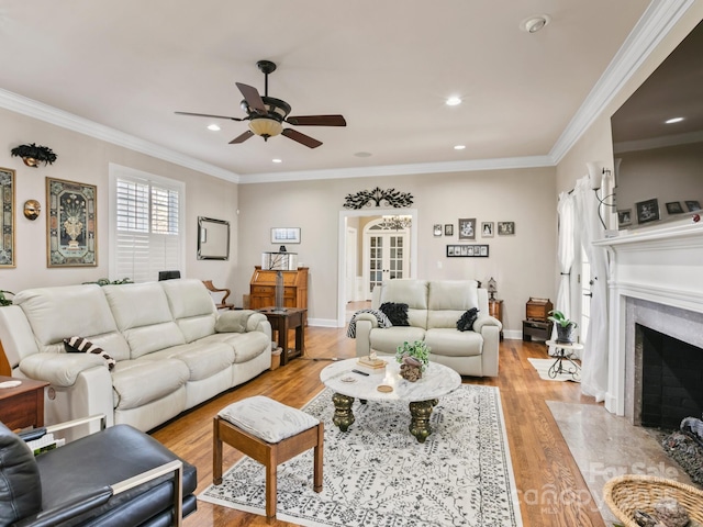 living area featuring baseboards, a ceiling fan, light wood-style flooring, ornamental molding, and a fireplace