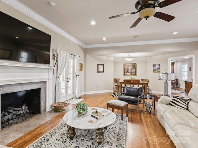 living area with baseboards, wood-type flooring, a premium fireplace, crown molding, and recessed lighting