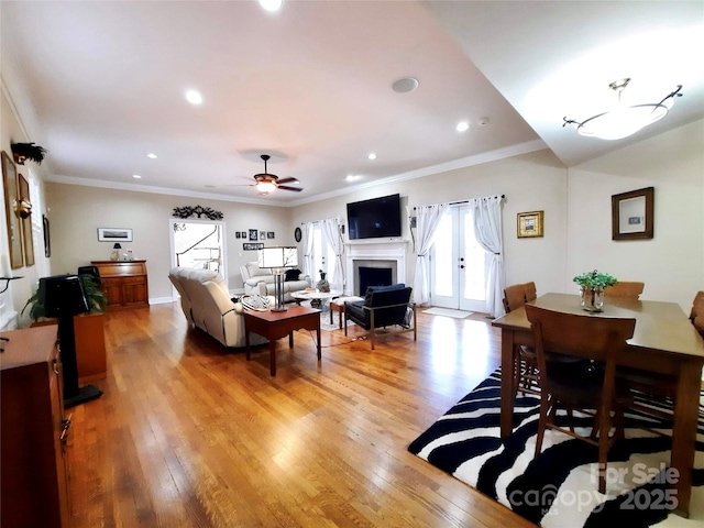 living area with light wood-style floors, a fireplace, a ceiling fan, and crown molding