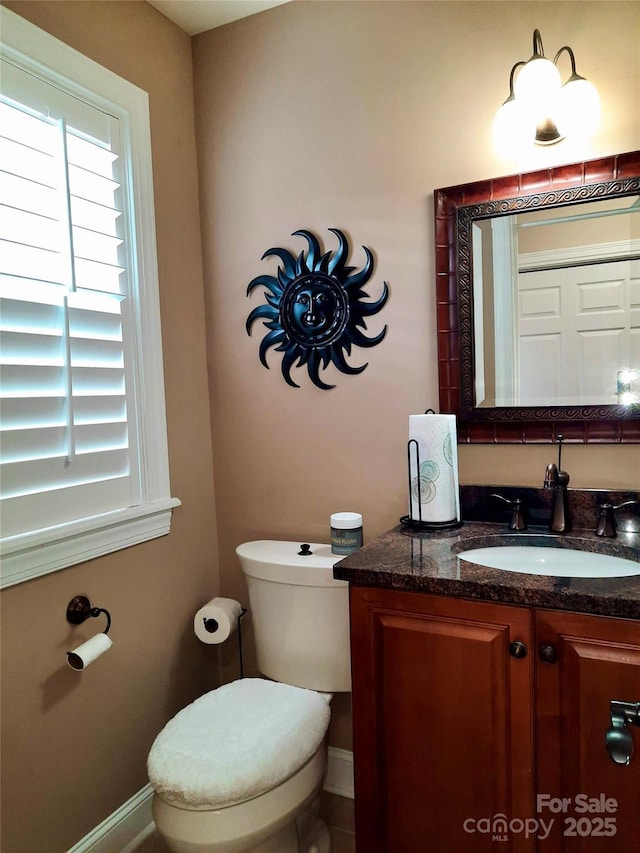 half bath with toilet, baseboards, and vanity