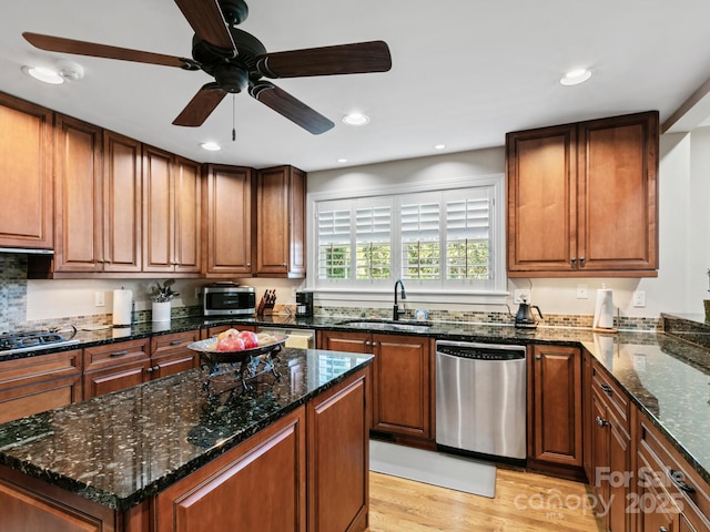 kitchen with stainless steel appliances, dark stone counters, a sink, and light wood finished floors