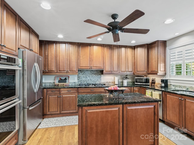 kitchen with dark stone counters, light wood-style flooring, appliances with stainless steel finishes, a center island, and recessed lighting