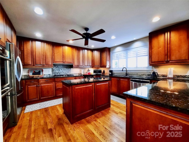 kitchen with dark stone counters, a kitchen island, appliances with stainless steel finishes, light wood-style floors, and a sink