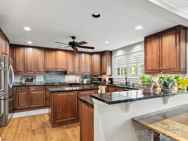 kitchen with a breakfast bar area, a peninsula, stainless steel appliances, a center island, and dark stone counters