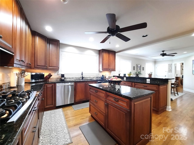 kitchen with stainless steel appliances, a peninsula, a kitchen island, a sink, and light wood-style floors