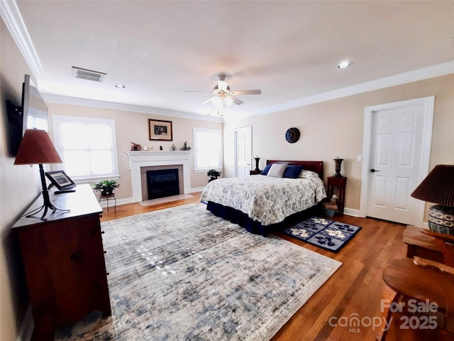 bedroom with baseboards, visible vents, crown molding, and wood finished floors