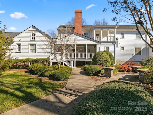 rear view of property with a sunroom, a lawn, a chimney, and a balcony