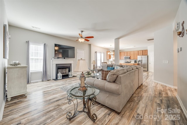 living area with a wealth of natural light, a fireplace with flush hearth, visible vents, and light wood-style floors