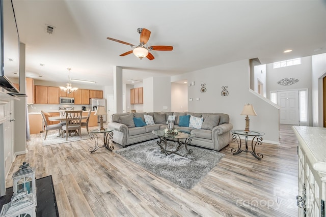 living room featuring light wood-style floors, baseboards, visible vents, and ceiling fan with notable chandelier