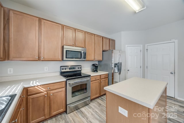 kitchen featuring stainless steel appliances, light countertops, a sink, a kitchen island, and light wood-type flooring