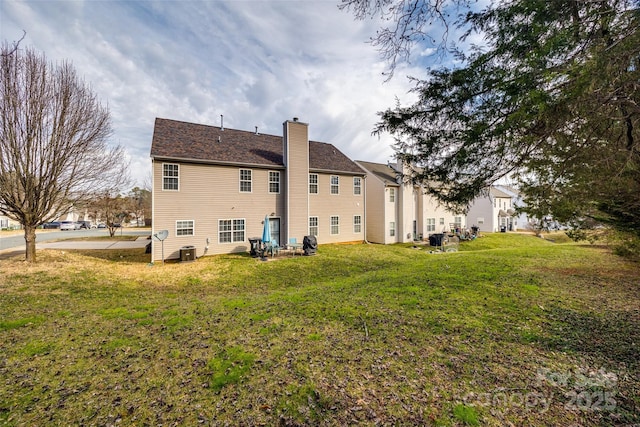 rear view of house featuring a chimney, a lawn, and central air condition unit