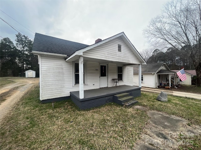 bungalow featuring an outbuilding, a chimney, a storage unit, a shingled roof, and covered porch